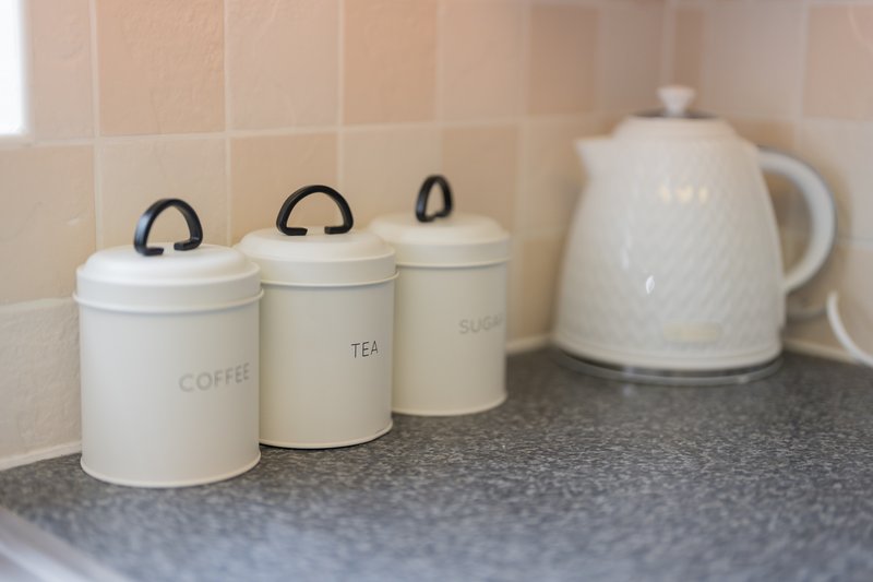 Kitchen counter with white ceramic storage canisters labeled coffee, tea, and sugar, plus electric kettle