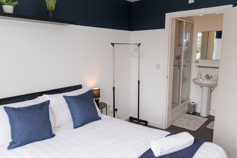Modern bedroom with double bed, blue pillows, dark headboard, ensuite bathroom visible