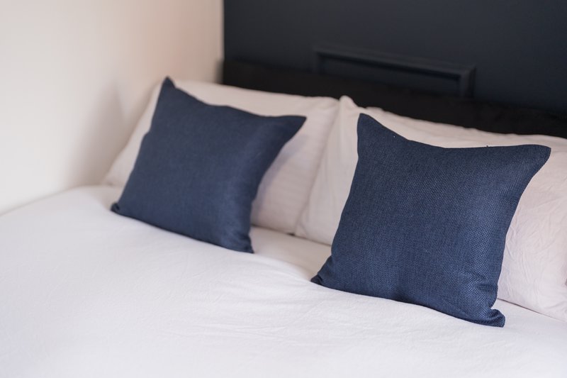 Bed with white linens, two navy blue cushions and white pillows