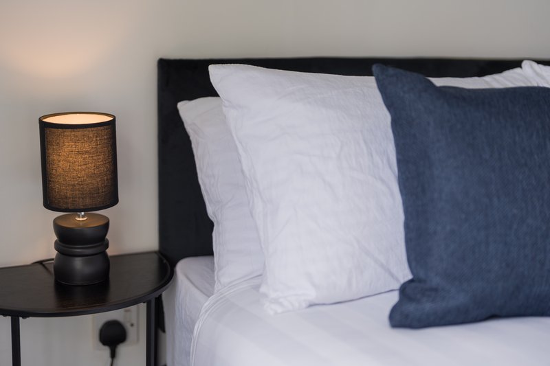 Bedroom bedside with table lamp, white and blue pillows on dark bed