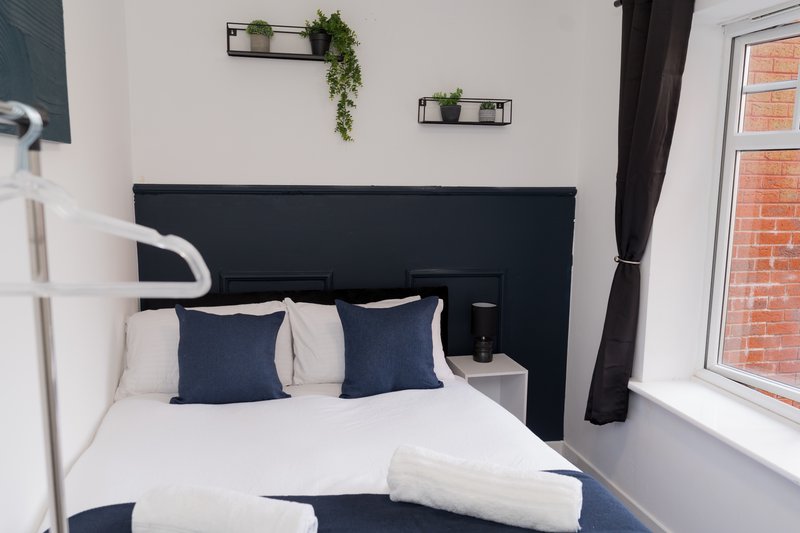 Modern bedroom with double bed, dark headboard, navy pillows and white bedding