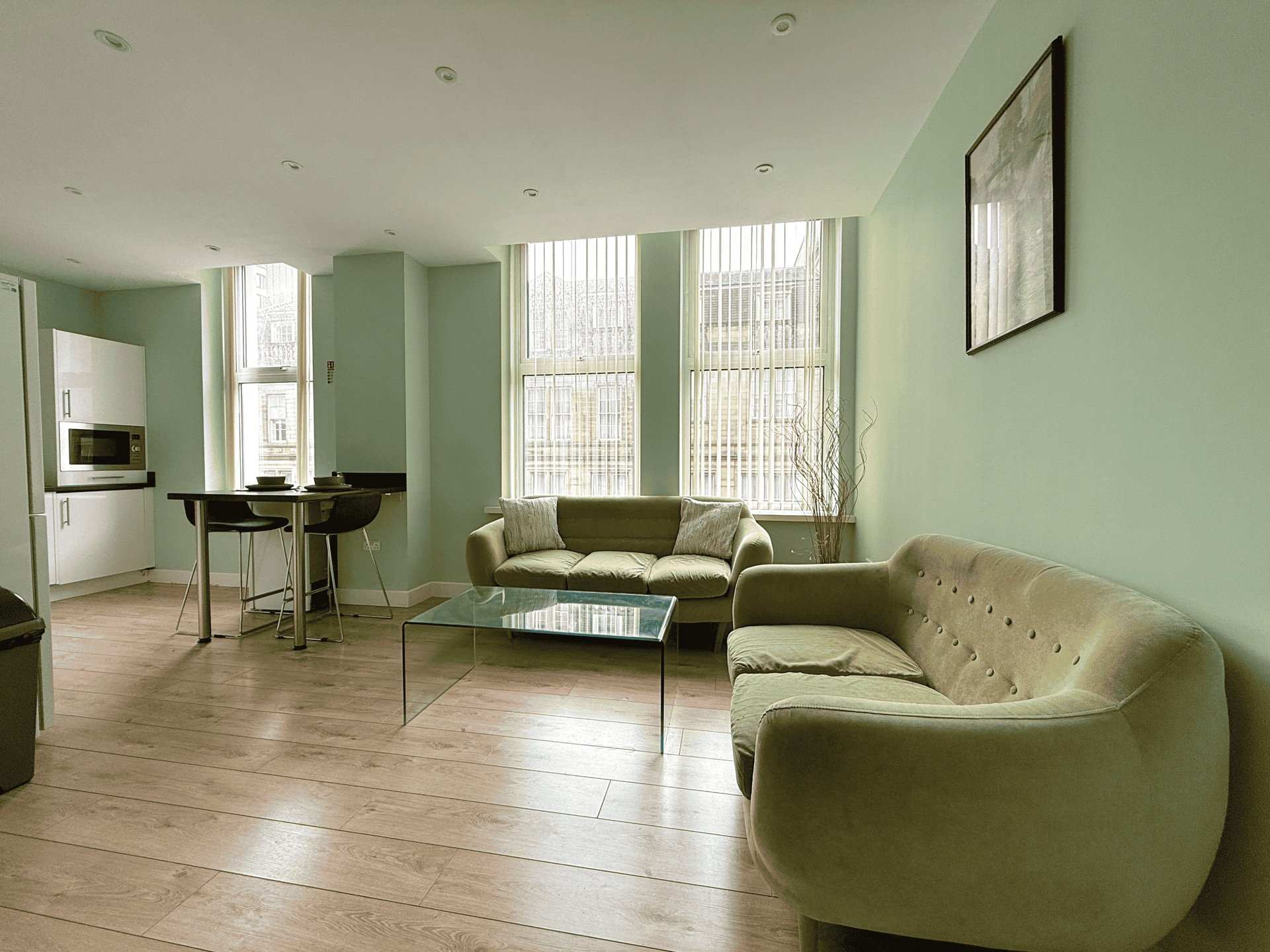 Open-plan living area with sage green walls, wooden flooring, contemporary furniture and large windows