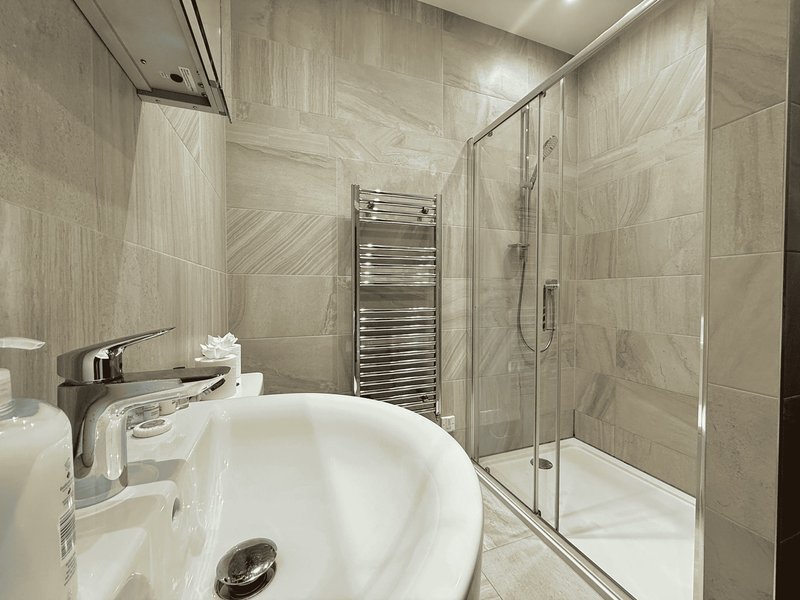 Modern bathroom with white circular sink, glass shower enclosure, heated towel rail and beige tile walls