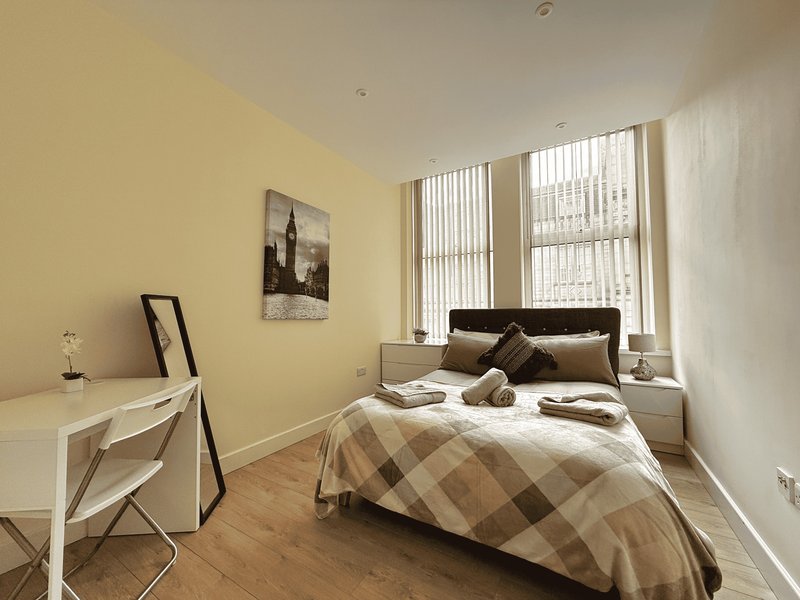 Bedroom with double bed, desk, yellow walls, wooden floor and large windows