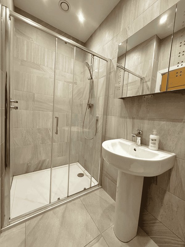 Modern bathroom with glass shower enclosure, pedestal sink, and tiled walls