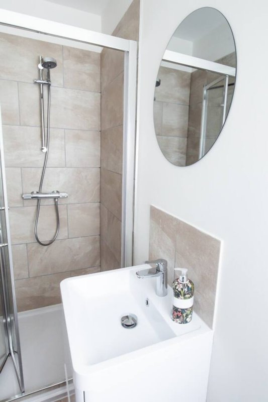 Modern bathroom with white sink, oval mirror, and walk-in shower with beige tile