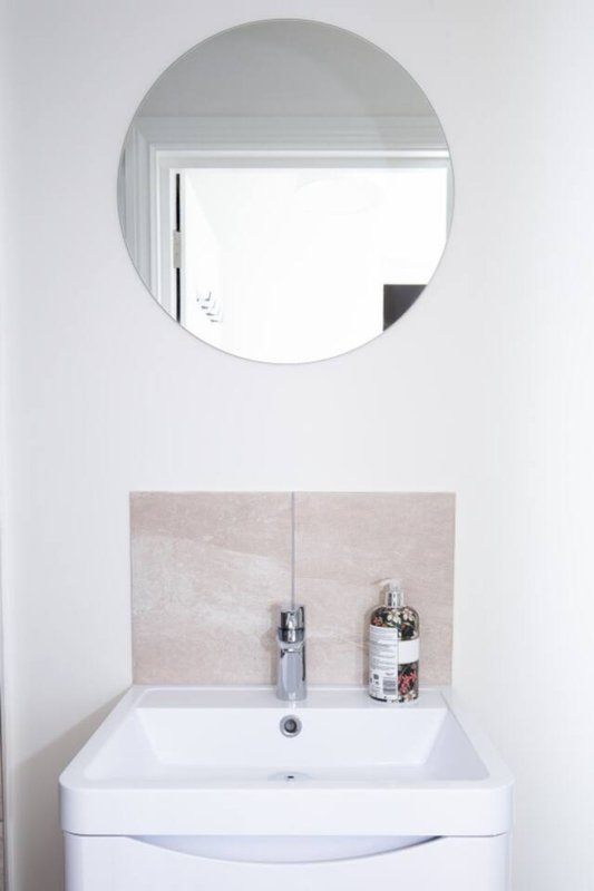 Bathroom sink with white vanity, round mirror, and tiled backsplash
