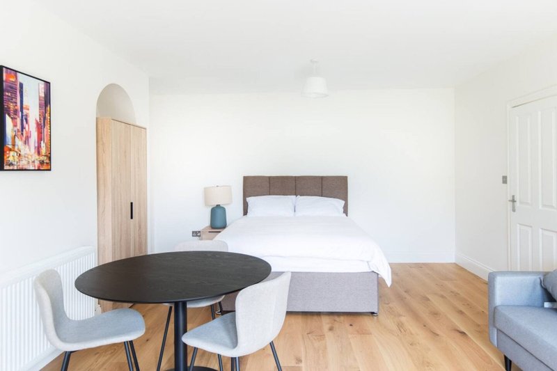 Bright bedroom with double bed, round black dining table, chairs, wooden floor and wardrobe