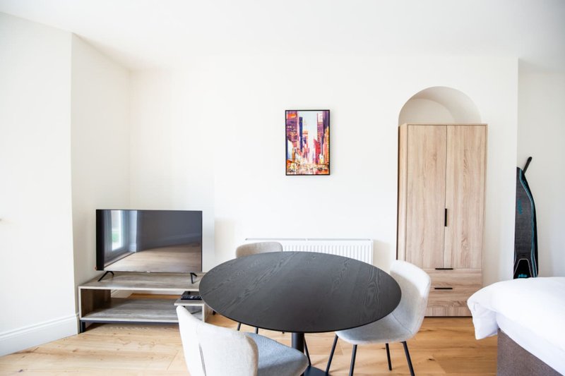 Modern bedroom with round black table, white chair, TV, wooden wardrobe and bed