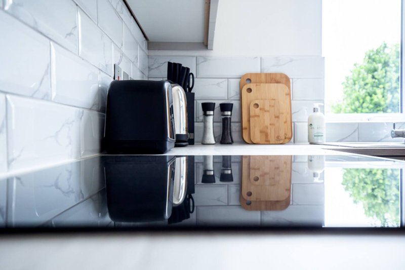 Kitchen countertop with white subway tile backsplash, black kettle, wooden cutting board, and small appliances