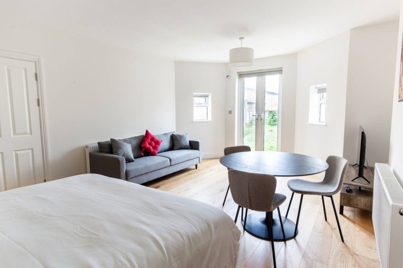 Modern studio apartment with bed, sofa, dining table and glass doors to garden