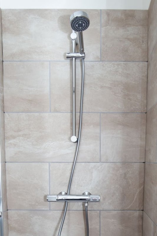 Bathroom shower wall with beige tile and chrome showerhead with handheld attachment