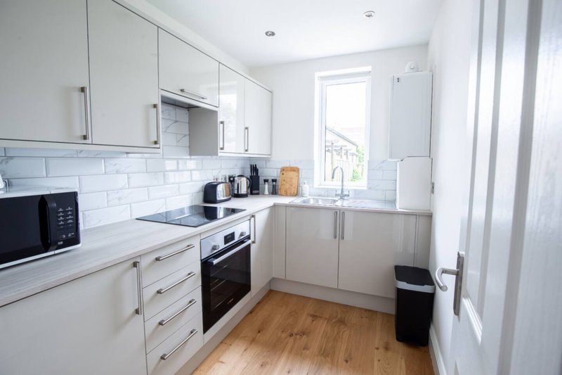 Modern white kitchen with built-in appliances, subway tile backsplash, wooden flooring and window