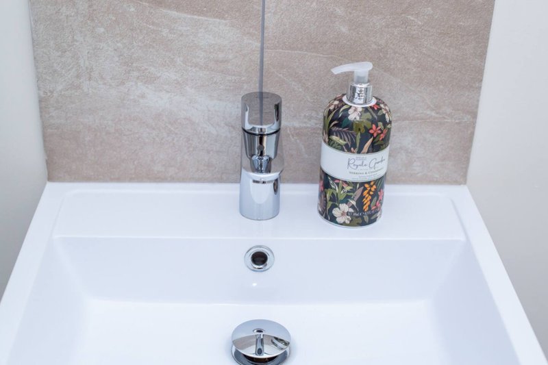 Modern bathroom sink with chrome faucet, soap dispenser, and decorative hand wash bottle