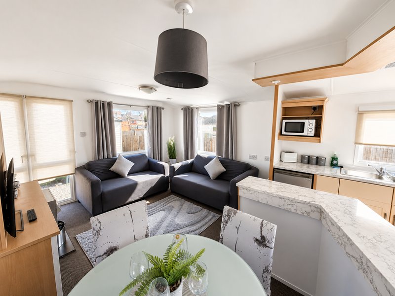 Modern open-plan living space with corner sofa, dining table, kitchen area and pendant lighting
