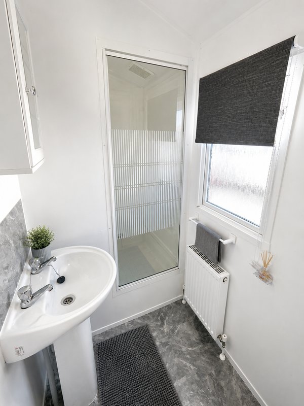 Small bathroom with white sink, shower enclosure, radiator and window with blind