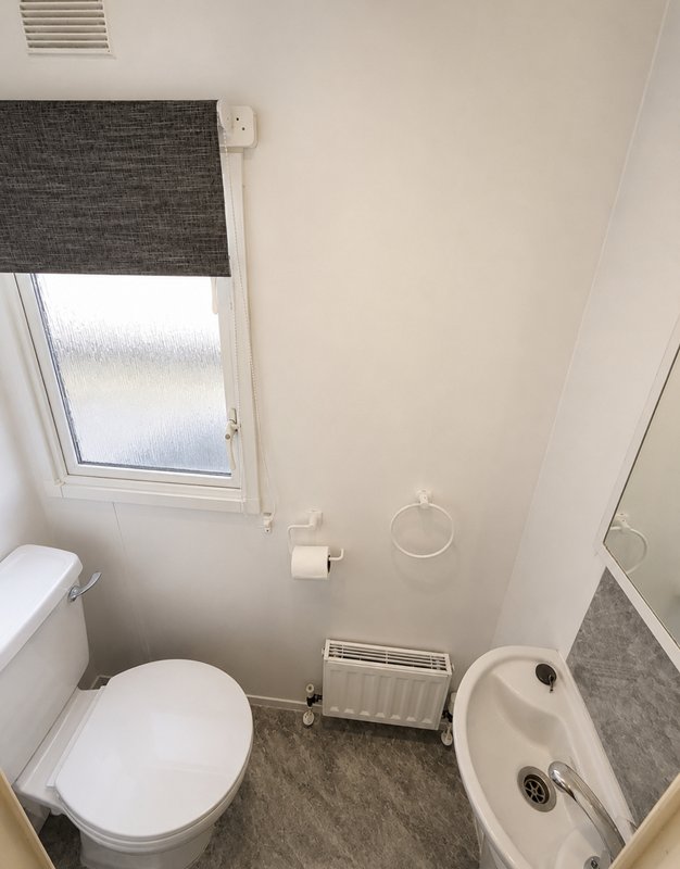 Small bathroom with toilet, sink, radiator and frosted window with dark roller blind