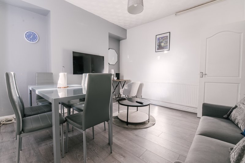 Modern living room with dining table, chairs, TV, and seating area with wooden flooring