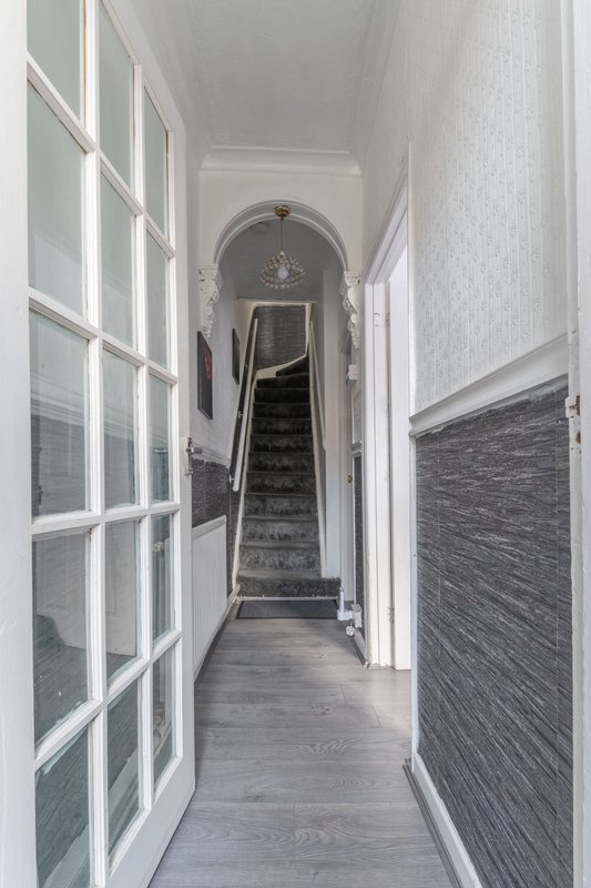 Narrow hallway with white walls, grey flooring, and staircase leading upward in distance