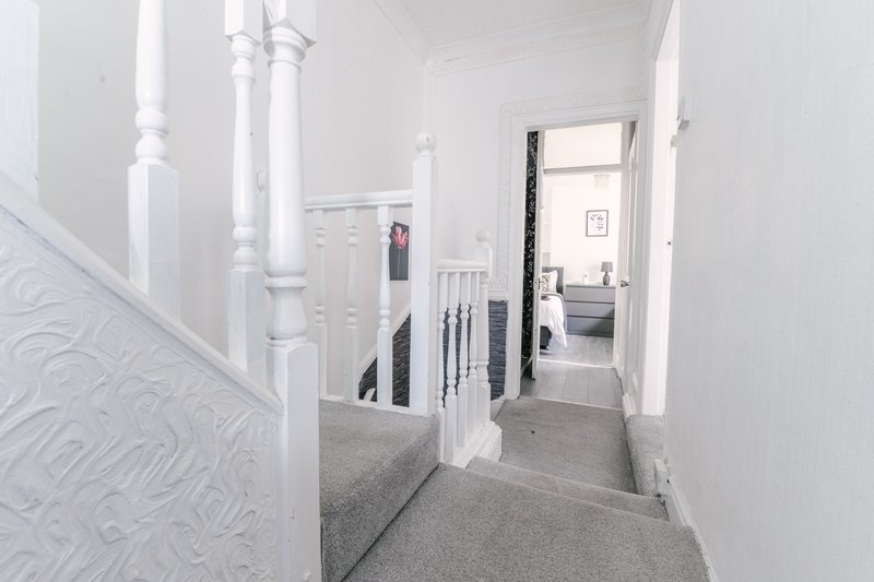 Bright hallway with white walls, staircase with black railings, grey carpet flooring