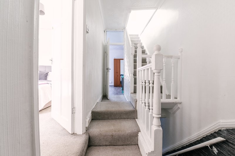 Bright hallway with stairs, white walls, wooden railings and grey carpet