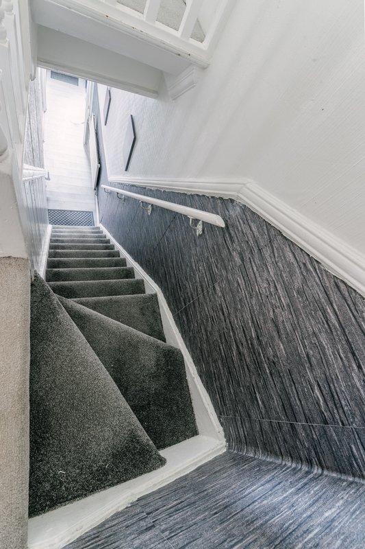 Staircase with gray and dark patterned carpet, white walls and wooden handrail