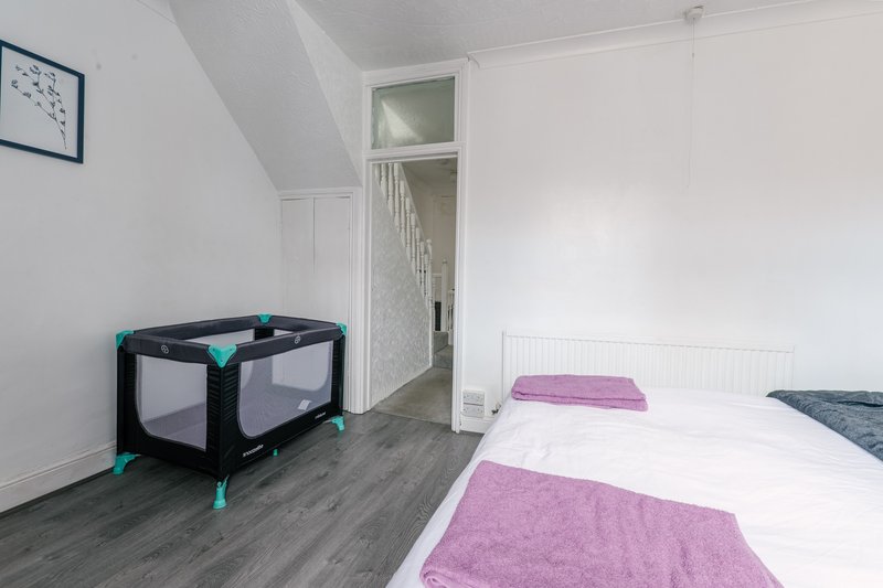 Bright bedroom with two single beds, purple throws, travel cot, and built-in wardrobe