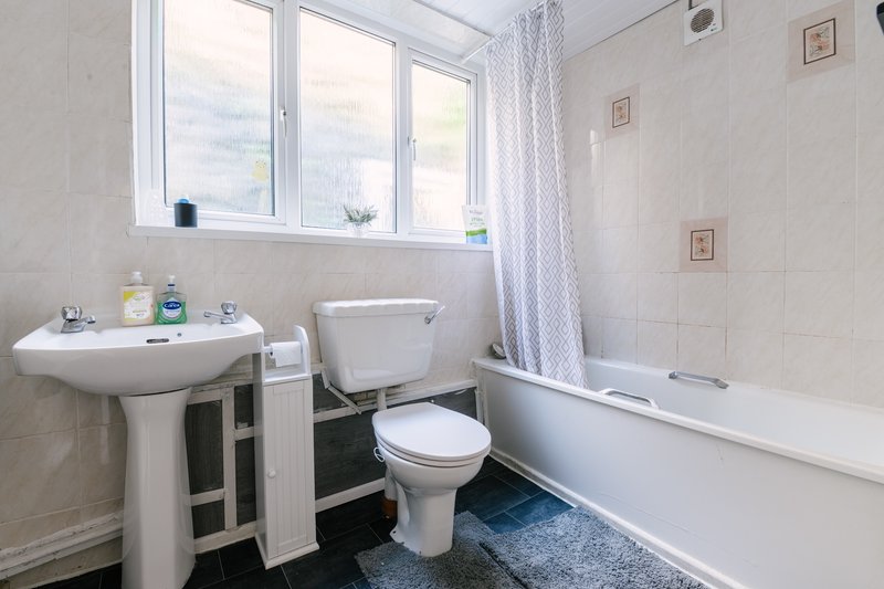 Clean bathroom with pedestal sink, toilet, bathtub, window and blue mat
