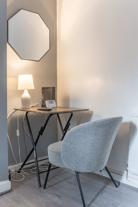 Modern desk area with grey upholstered chair, octagonal mirror, and table lamp
