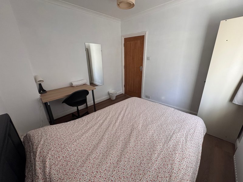 Bright bedroom with double bed, desk, mirror and wooden door