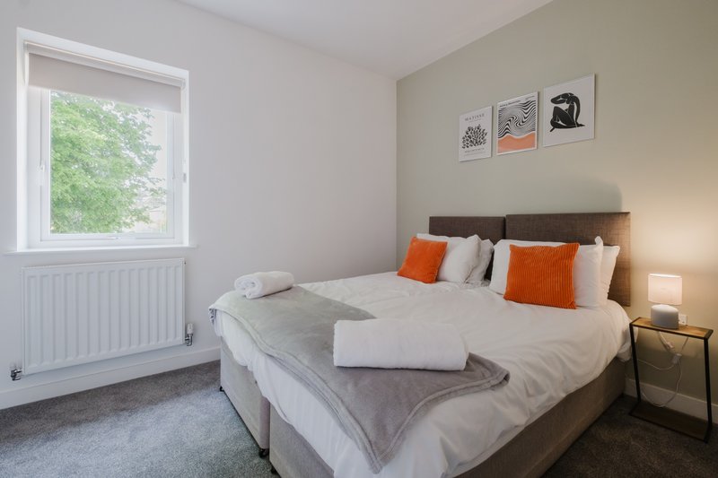 Bright bedroom with double bed, orange cushions, window view and wall art