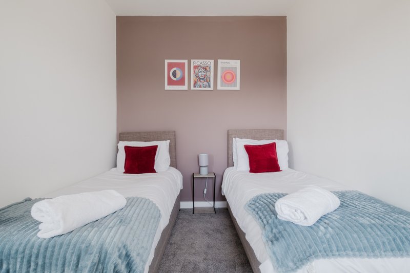 Twin bedroom with two single beds, red cushions, white bedding, and framed wall art