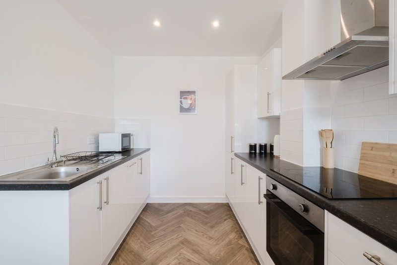 Modern white kitchen with black countertops, herringbone flooring, and stainless steel appliances