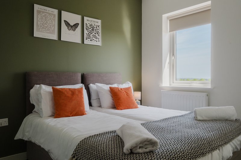 Modern bedroom with double bed, orange cushions, green walls and framed artwork