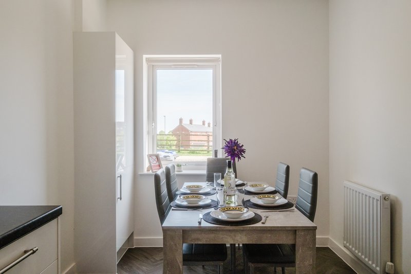 Dining room with wooden table, place settings, purple flowers, and view through glass doors to exterior