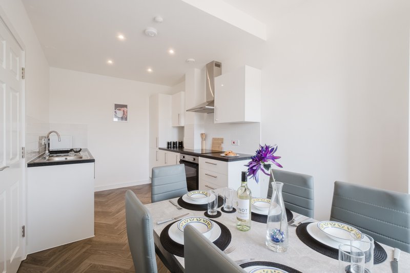 Modern open-plan kitchen and dining area with white cabinetry, dining table set for four, and purple flowers in vase