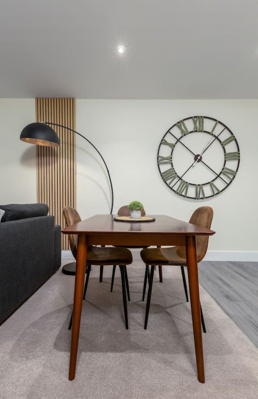 Modern living space with wooden dining table, black chairs, arc lamp, and large wall clock