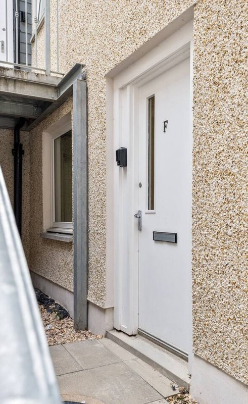 Modern white entrance door on cream rendered exterior wall with gravel driveway