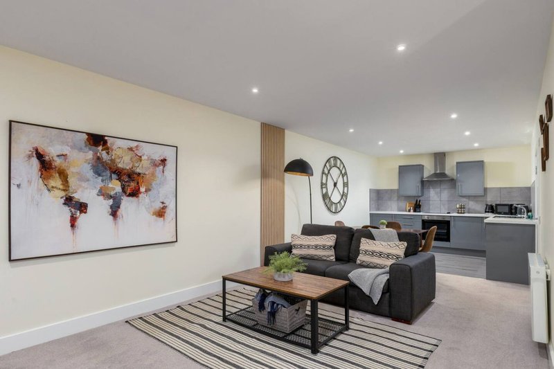 Modern open-plan living area with world map artwork, black sofa, striped rug and kitchen beyond