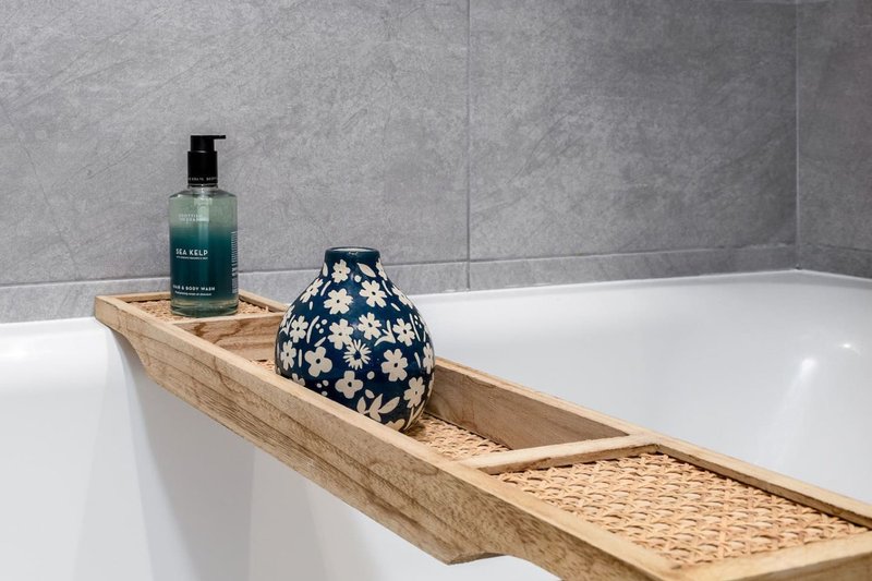 Modern bathroom with white bathtub, wooden bath caddy holding soap bottle and decorative bowl