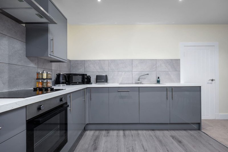 Modern kitchen with grey cabinetry, white countertop, black oven and grey tile backsplash