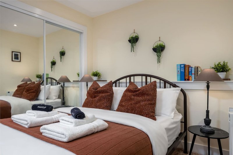 Modern bedroom with double bed, brown cushions, white bedding, mirror wardrobe and floating shelves