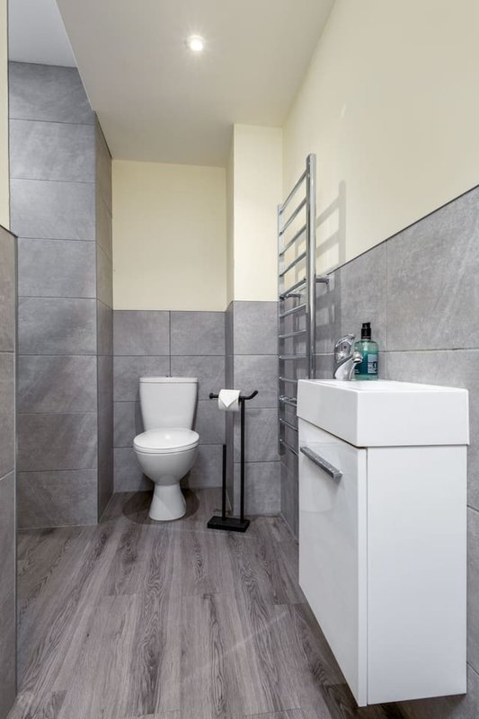 Modern bathroom with white vanity, toilet, heated towel rail and grey tile walls