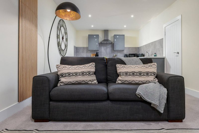 Modern living room with dark sofa, patterned cushions, arc lamp and open-plan kitchen beyond