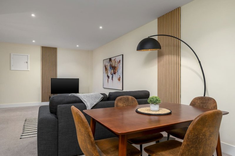 Modern open-plan living and dining area with dining table, upholstered chairs, grey sofa, and arc lamp