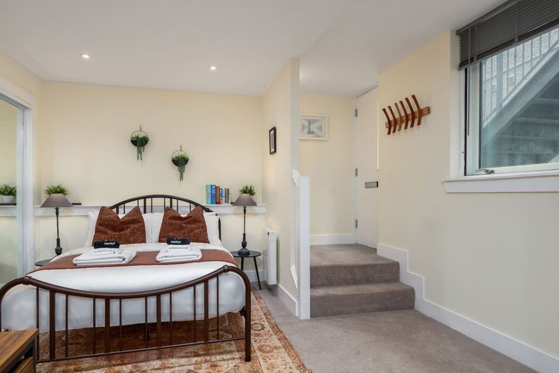 Bright bedroom with metal-frame bed, wooden headboard, cream walls and carpeted stairs visible