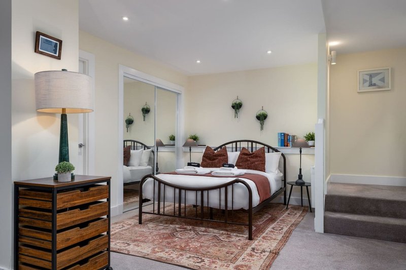 Bright bedroom with metal bed frame, burgundy cushions, wooden dresser and table lamp
