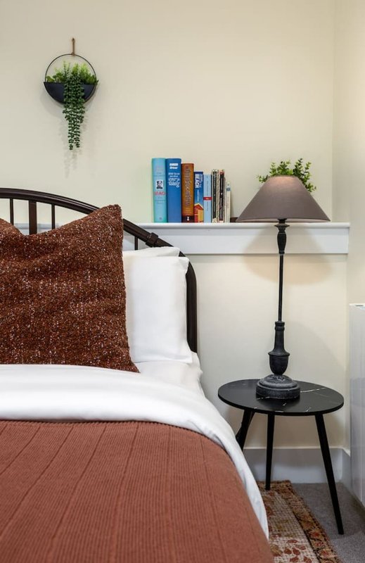 Bedroom with bed, bedside table, lamp, books, and hanging plant decoration