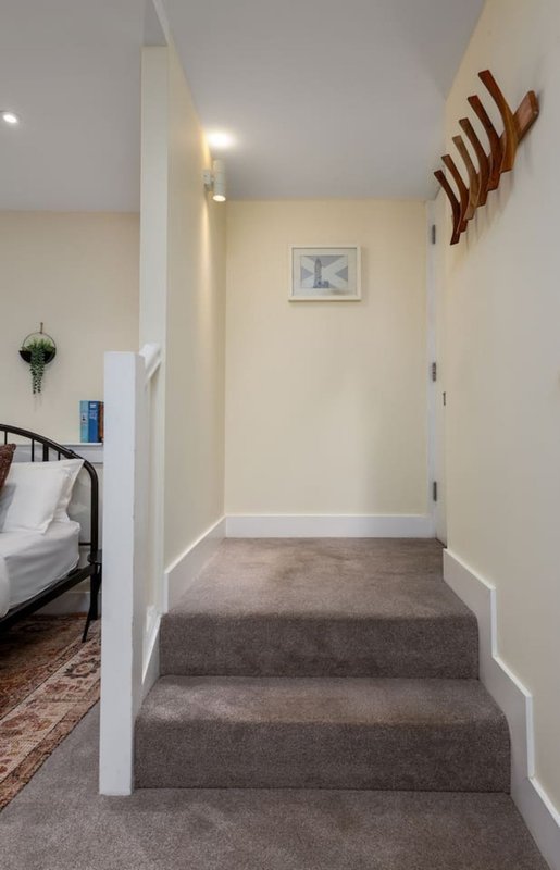 Hallway with carpeted stairs, cream walls, white trim, wooden wall rack and bedroom visible left