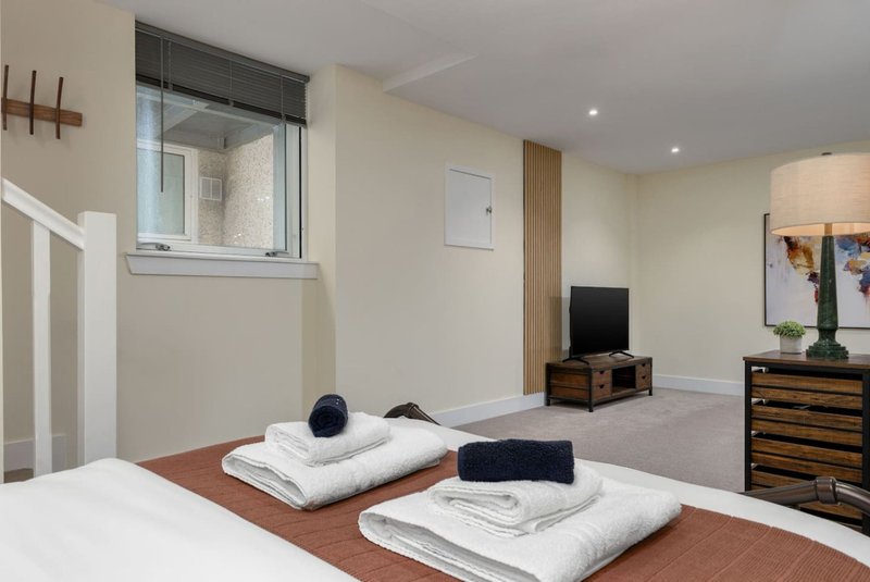Spacious bedroom with two beds, wooden dressers, TV, window and carpeted floor